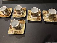 Five espresso cups each paired with matching square saucer, arranged on a dark surface.