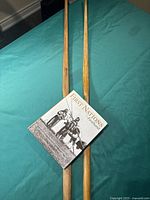 Book 'First Nations - Fifteen Centuries' with dust jacket, showing cover and title, positioned over two longbows on green surface.