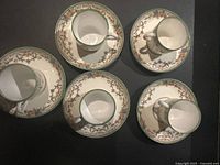 Top-down photo of five porcelain espresso cups placed on matching saucers showing floral pattern and green border.