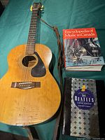 Yamaha acoustic guitar with Beatles book and Encyclopedia of Music in Canada side by side on a blue cloth surface.