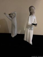 Front angle photo of the white porcelain figurine held by a young girl, wearing a long white dress and holding a candle holder.