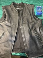 Front view of black leather vest showing zipper closure and two front pockets, minor creases visible on leather surface.