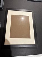 Single black frame with white mat on dark surface, slight reflections on glass part.