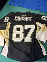 Back of black Reebok hockey jersey with 'CROSBY' and number 87 in white outlined letters, size appears to be Small/Medium Youth.