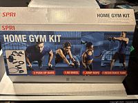 Original boxed SPRI Home Gym Kit showing included items: 2 push-up bars, 1 ab wheel, 1 jump rope, 1 resistance tube.