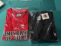 Red University of Guelph Colosseum Athletics jersey size S in packaging next to navy blue Toronto Maple Leafs vest folded in packaging.