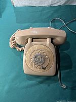 Top view of beige rotary dial telephone showing full rotary dial, handset resting on cradle, and coiled handset cord.