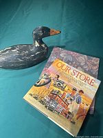 Side view of the medium wooden duck decoy showing paint wear and handmade details alongside two books.