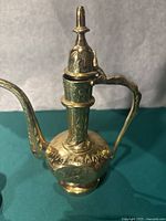 Close-up of the vintage brass teapot showing its engraved floral patterns on body, neck, lid and handle.