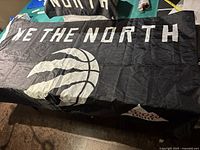 Flag laid out flat showing 'We The North' text and basketball graphic printed in white on black background.