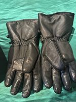 Pair of black leather motorcycle gloves laid flat showing gauntlet-style design with elastic at the wrist and smooth leather finish.