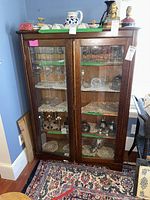 Front view of a wooden antique china cabinet with two glass doors showing interior glass shelves and various glassware inside.