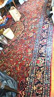 Full view of red and navy floral area rug with surrounding items