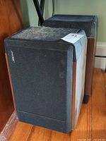 Pair of two Bose bookshelf speakers showing black cloth grille and wood grain side panels. Top surfaces covered in pet hair and dust.