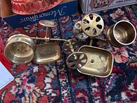 Brass toothbrush holder, soap dish, finials and a round brass cup displayed on floor with patterned carpet
