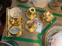 Top-down view showing sugar bowl, creamer, salt and pepper shakers on gold tray with spoon, plus two gold candle holders and additional items on table surface.