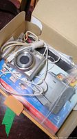 Open box showing Canon PowerShot A570 IS camera with USB/AV cables, wrist strap, manuals, and original packaging.
