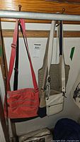 Five crossbody purses hanging on hooks showing full front and side views in assorted colors and materials.