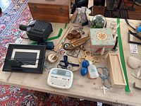 Full view of table with all items spread out including digital picture frame, label maker, rosary beads, glass terrarium, pulse oximeter, stone bookends, wooden and ceramic boxes and trays.