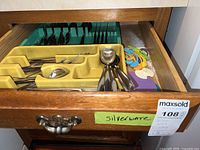 Drawer with several yellow and green utensil organizers holding multiple pieces of stainless steel flatware including spoons, knives, forks and colorful plastic bag clips.