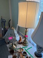 Two brass base lamps with different shades on a table, one with beige cloth shade about 37 inches, one with floral stained glass shade about 22 inches.