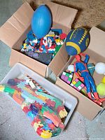 Overall view of boxes containing Lego bricks, Spiderman figure, balls, Rubik's Cubes, and puzzle pieces.