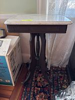 Front side view of marble top table with wood base, showing central pedestal and four legs on castors.