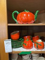 Pumpkin-shaped teapot on top shelf and orange plates and cups with sugar bowl and creamer on bottom shelf.