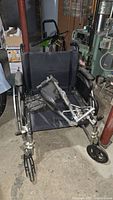 Full view of black Medline folding wheelchair with footrest attachments on the seat, indoors on concrete floor near basement utility area.