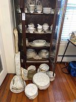 Cabinet view of Royal Doulton china sets on wooden shelves with vinyl storage boxes and lace doilies on floor