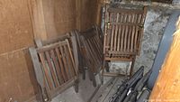 Group of folded teak chairs leaning against a wooden wall