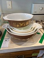 Stacked view of four brown Pyrex mixing bowls with white interiors and gold decorative patterns showing wear and fading. Items placed on kitchen counter near stove.