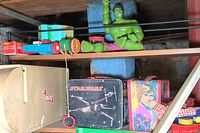 Shelf with vintage lunch boxes, a wooden toy train, green Hulk action figure, and other assorted toys