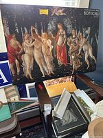 Large Botticelli print leaning against wall surrounded by other art prints and frames