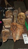 Wide view of six wooden spirit face carvings arranged on a table showing diverse expressions and natural wood textures.