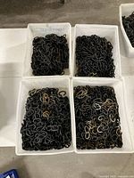 Four white bins filled with heavy duty black 4 gauge chains, some links chrome or brass plated, chains coiled inside