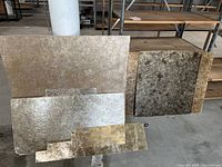 Photo showing several amber mica sheets stacked vertically leaning against a pillar and bench, including two large full sheets, one medium sheet, and partial sheets visible behind.