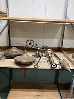 Photo showing several metal lamp parts including round lamp shades, pull chain, and finial on a warehouse shelf