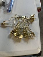 13 gold-tone metal clip-on lampshade holders arranged on a white surface, including various sizes of adapter clips.