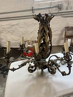 Full view of the brass chandelier placed on a table showing six candle-style light arms and ornate leaf motifs.