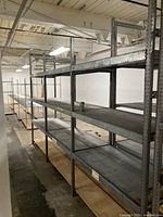 Long view of assembled metal shelving showing multiple adjustable shelves with plywood base in a warehouse environment.