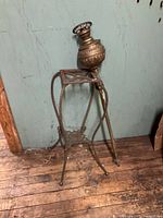 Full view of the brass oil floor lamp showing the ornate brass oil reservoir and the three-legged stand with one leg damaged.