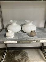 Pair of large milk glass lamp shades with a small hobnail glass shade and a small frosted glass shade, all displayed on metal shelving.