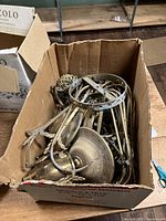 Box filled with assorted brass chandelier parts including arms, central stem pieces, and decorative elements.