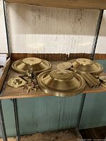 Three large brass ceiling mount plates with accompanying brass rods and sockets arranged on a shelf