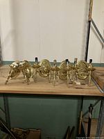 Five brass sconces on a wooden shelf including two single-arm pairs, one double-arm pair, and one sconce for parts.