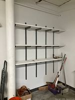 Wall shelving system installed showing three white wooden shelves supported by metal brackets and vertical tracks mounted on a wall