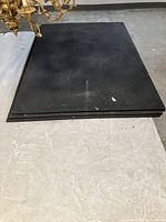 Stack of four black rubber mats on concrete floor, chandelier portion visible in corner.