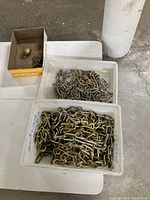 Overview of two bins containing welded metal chains with large and small links, plus a small cardboard box with metal parts