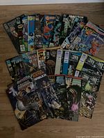 Top-down image showing full spread of 23 assorted comic books fanned out on floor, featuring colorful covers with characters including Superman and Spider-Man.